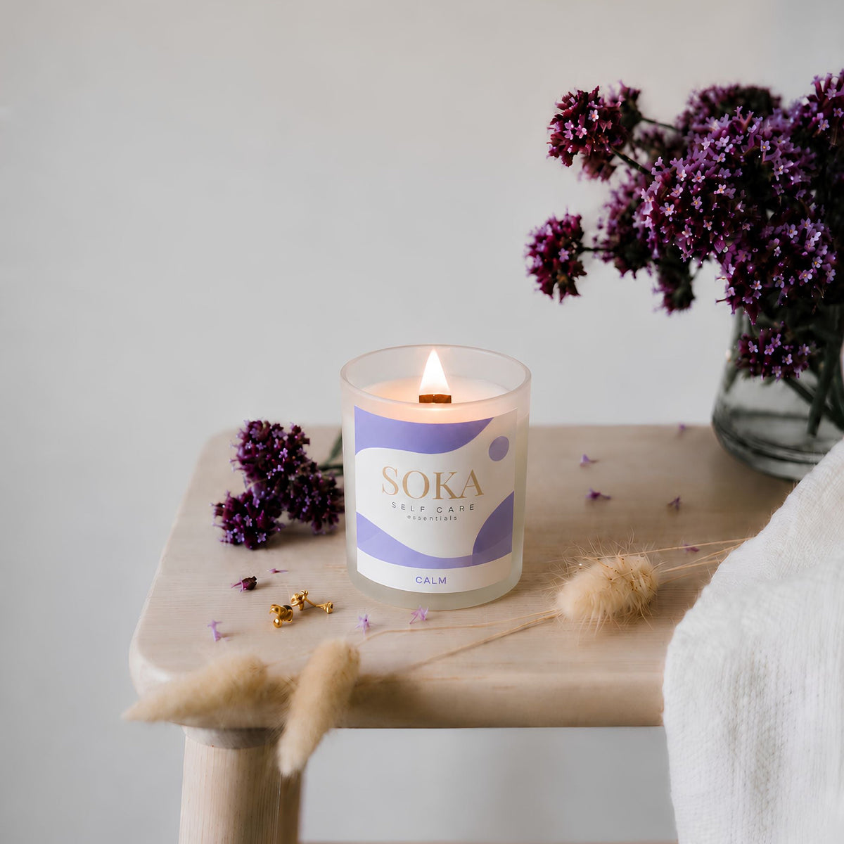 CALM Soka candle on a wooden table with flowers and decor elements.