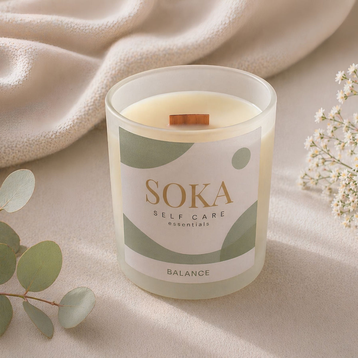 BALANCE Soka self-care candle on a soft beige background with eucalyptus leaves and flowers.