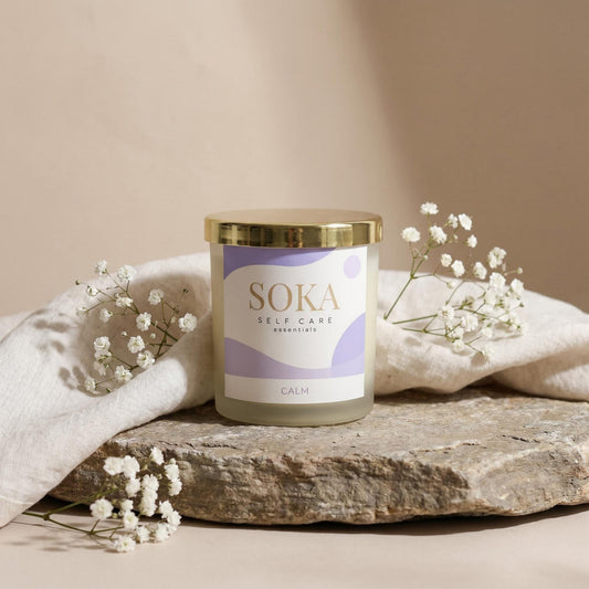 CALM Soka self-care candle on a stone surface with white flowers and a beige background