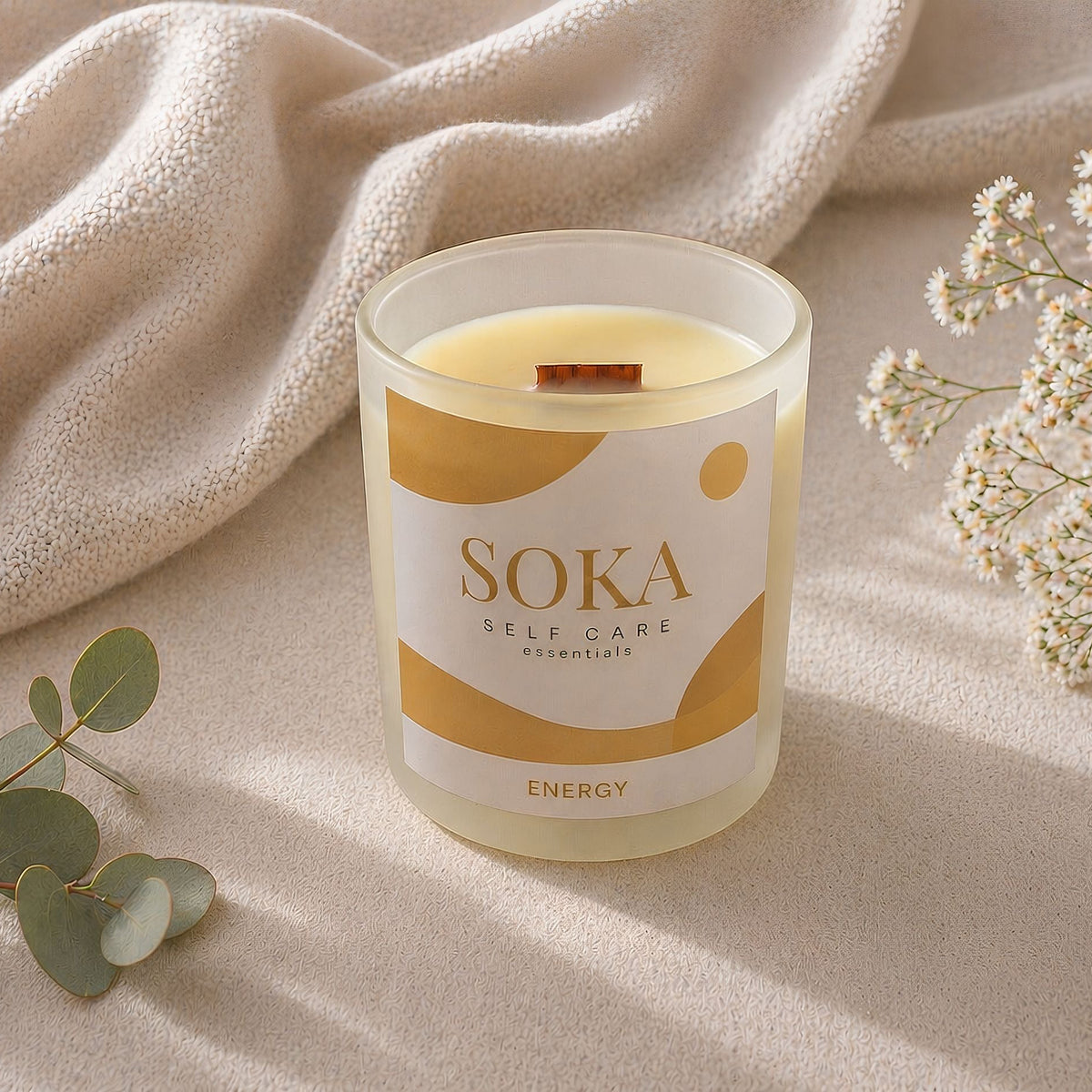 Soka candle labeled 'Energy' on a textured surface with flowers and leaves.