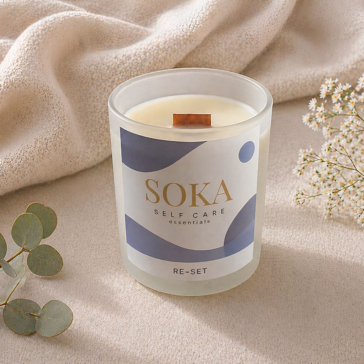 RE-SET Soka self care candle on a soft fabric background with eucalyptus and flowers.